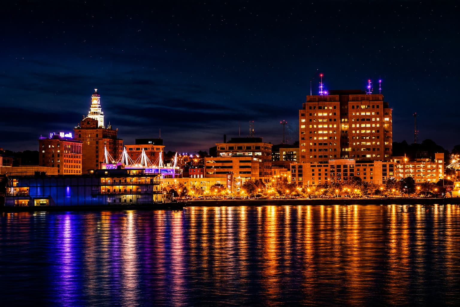 The Davenport, Iowa riverfront skyline at night, lights reflecting on the Mississippi